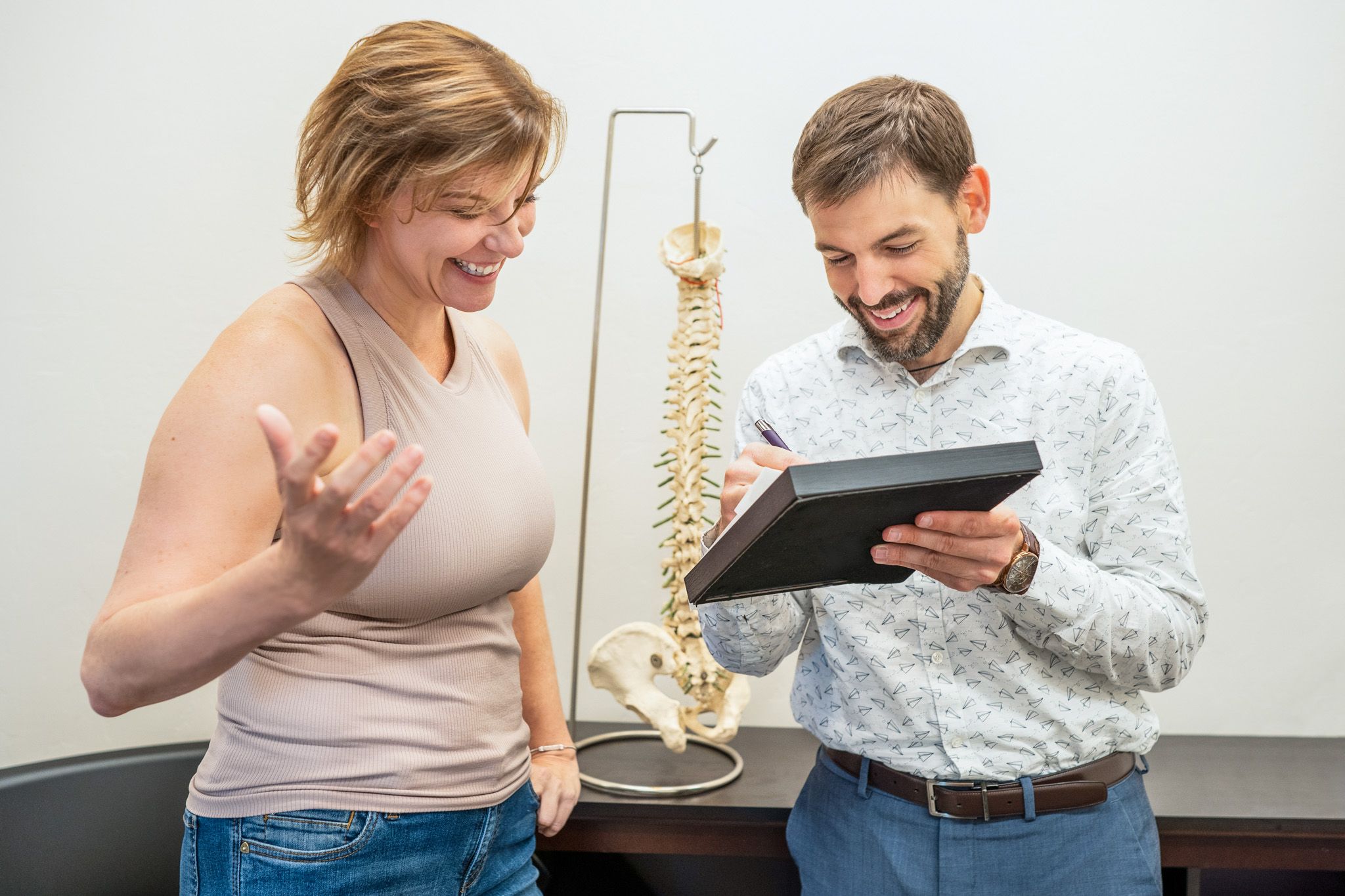 Chiropractor showing chart to female patient with hanging spine in background